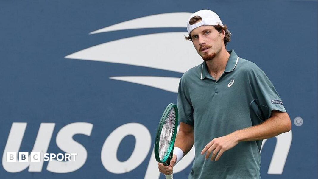 Rezultati US Opena 2026.: Toby Samuel zaradio prvu pobjedu u glavnom žrijebu Grand Slam turnira, ali Cameron Norrie pati prijevremeno odustajanje Toby Samuel, wearing a grey polo shirt and backwards white cap, holds his green racquet in his right hand